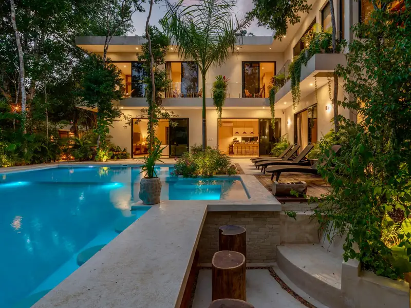 Piscina iluminada ao entardecer em jardim tropical